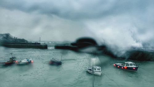 Boats sailing in sea against cloudy sky