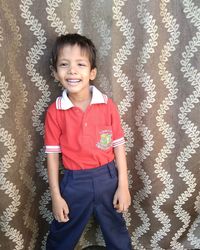 Portrait of smiling boy standing against curtain