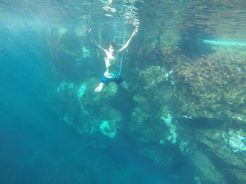 Shirtless teenage boy with arms raised in sea