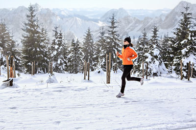 Woman running on snow covered field against trees