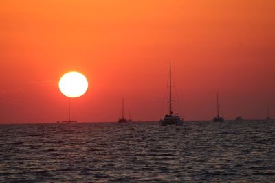 Silhouette sailboat sailing on sea against orange sky