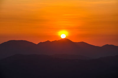 Scenic view of silhouette mountains against orange sky