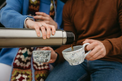 A man and woman drinking tea from thermos during autumn travel, couple holding handmade cups