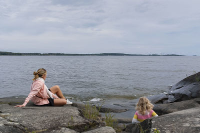 Woman sitting on rock by sea against sky