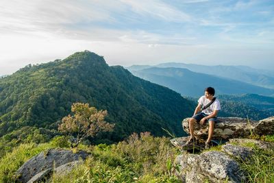 Man looking at mountain while sitting on cliff against sky