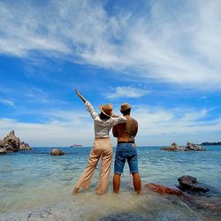 Rear view of men standing on rock by sea against sky