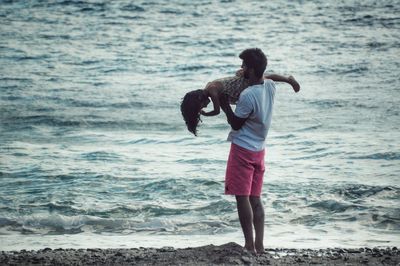 Full length of father carrying daughter at beach