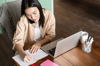 Young woman using mobile phone while sitting on table