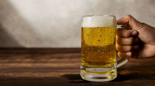 Close-up of hand holding beer glass on table