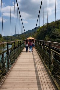 Rear view of woman on footbridge against sky