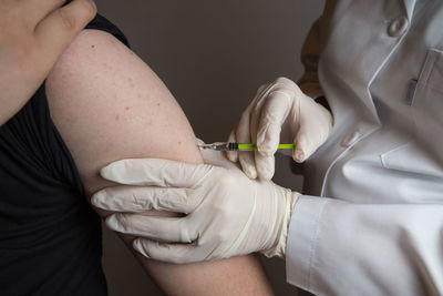 Midsection of doctor injecting syringe to patient against gray background