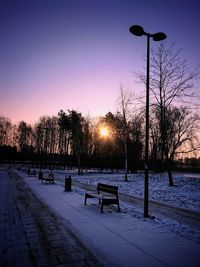 Snow covered street against sky during sunset