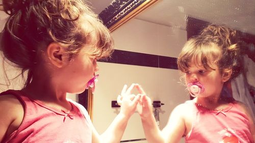 Reflection of cute girl sucking pacifier in mirror at home