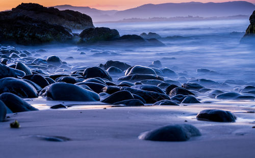 Rocks on beach against sky during sunset