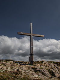 Low angle view of cross on rock against sky