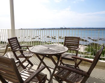 Empty chairs and table by sea against sky