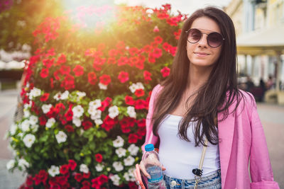 Young woman wearing sunglasses standing against pink flower