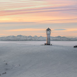 Lighthouse by sea against sky during sunset