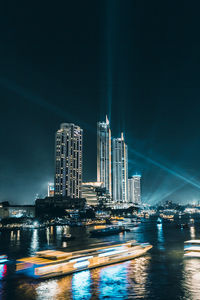 Illuminated buildings by river against sky at night