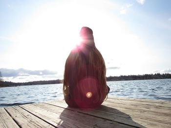 Rear view of woman sitting on pier against lake