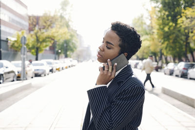 Young woman looking away while standing on street in city