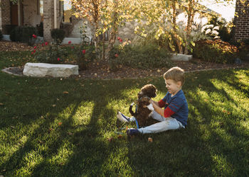 Happy boy playing with dog on grassy field in backyard