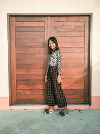 Full length portrait of woman standing against door