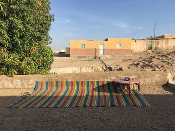 Carpet and table on field against trees and houses during sunny day