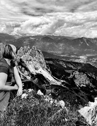 Woman sitting on rock looking at mountains against sky