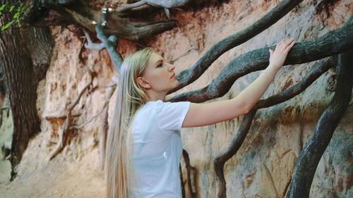 Side view of young woman standing by tree trunk