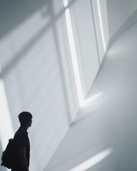 Side view of man with backpack standing against white wall