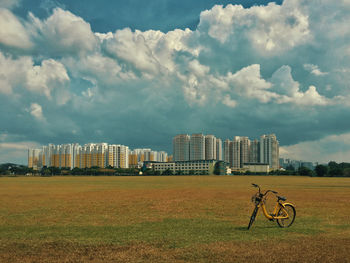 Bicycle on field by cityscape against sky