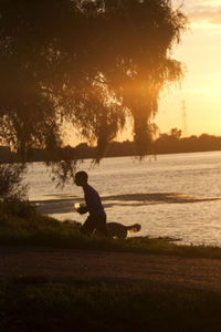 Boy with dog at lake against sky during sunset