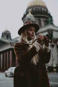 Portrait of woman with hat standing against built structure