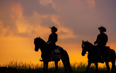 Three men dressed in cowboy garb, with horses and guns. a cowboy riding a horse in the sunset.