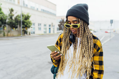 Young woman wearing sunglasses using smart phone on road