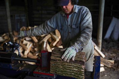 Hydraulic log splitter blade cuts into wood with workman and woodpile