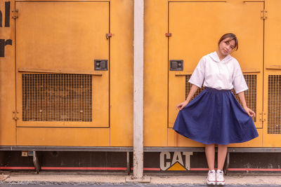 Portrait of smiling young woman standing against yellow wall