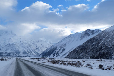 Road by snowcapped mountains against sky during winter