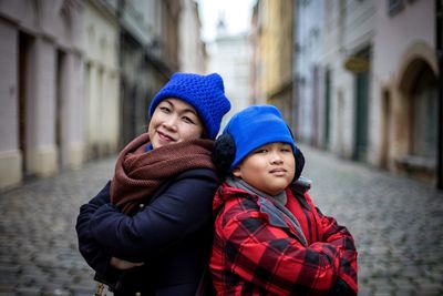 Portrait of smiling mother and son standing with arms crossed amidst buildings at city