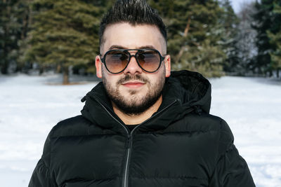 Portrait of young man wearing sunglasses while standing on snow