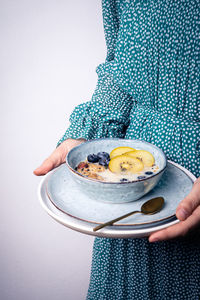 Crop anonymous female in dress carrying bowl of healthy granola mixed with milk blueberry and slices of kiwi for breakfast