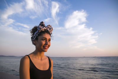 Young woman smiling at beach against sky