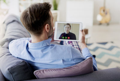 Rear view of man using mobile phone while sitting on sofa at home