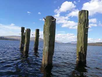 Wooden posts in lake against sky