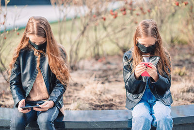 Girls with masks using mobile phone while sitting outdoors