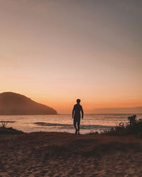 Silhouette man standing at beach against sky during sunset