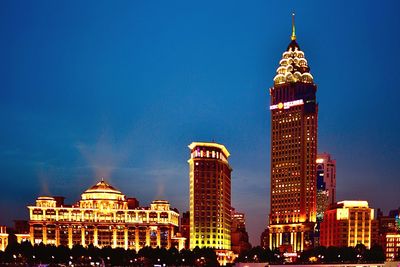 Illuminated buildings against blue sky at night