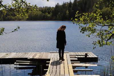 Rear view of woman standing on pier over lake