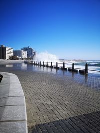 Footpath by sea against clear blue sky